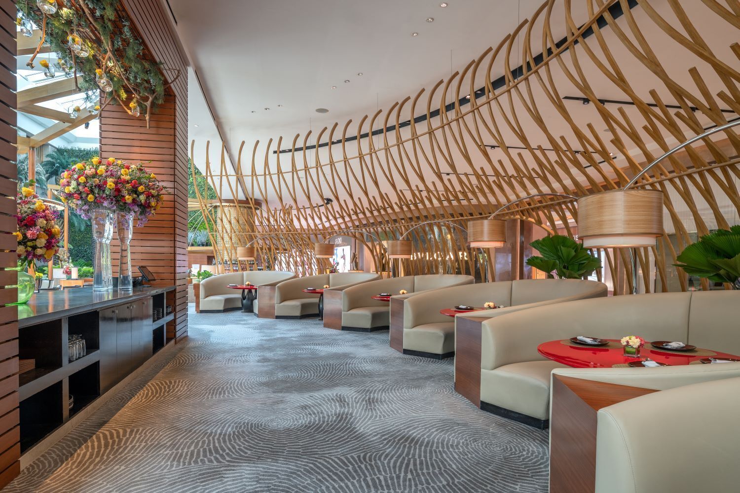 A modern hotel lobby with a unique bamboo ceiling design, plush seating, and a patterned carpet.