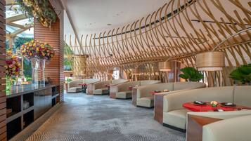 A modern hotel lobby with a unique bamboo ceiling design, plush seating, and a patterned carpet.