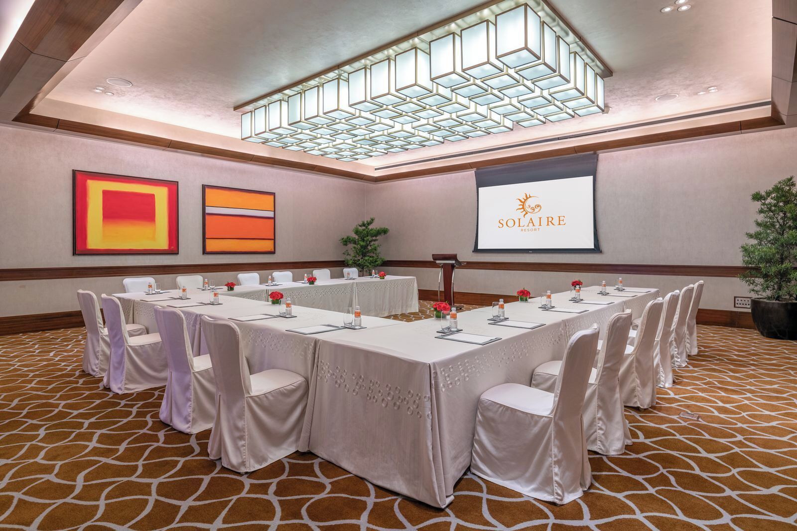 A conference room with a long table, white chairs, and a large screen displaying "SOLAIRE RESORT".