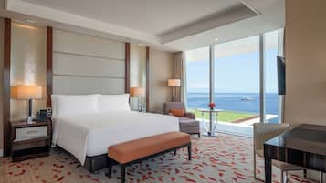 A hotel room with a large bed, a desk, a chair, and a view of the sea.