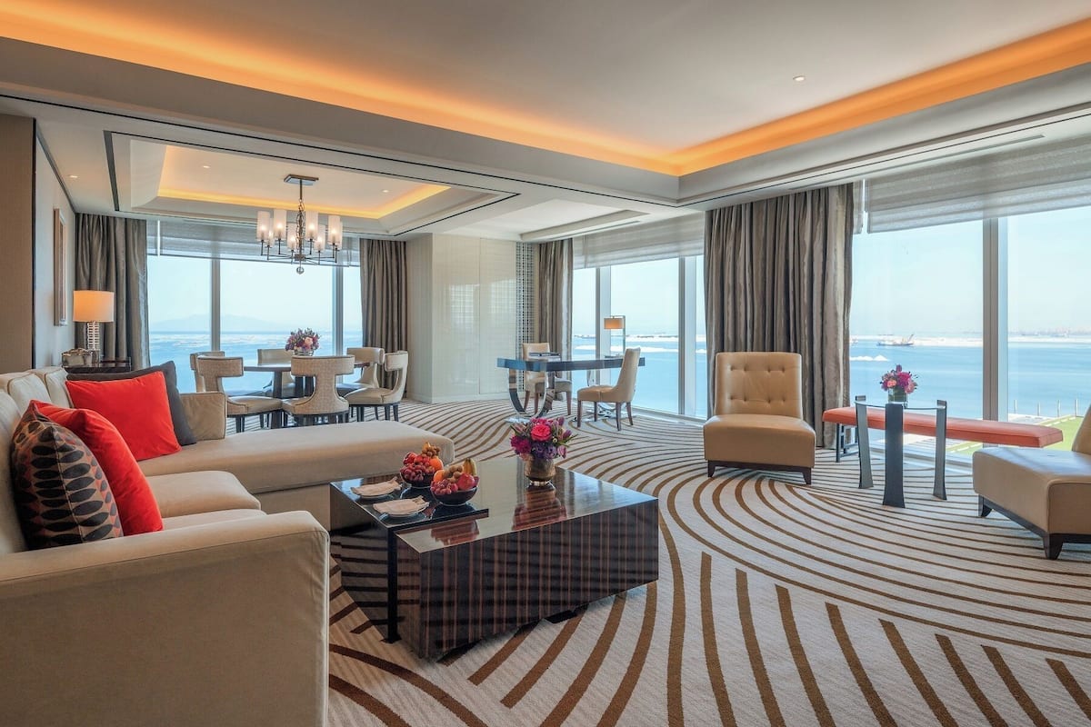 Une chambre d’hôtel moderne dotée d’un grand lit, d’un coin salon avec une table basse et d’une vue sur la mer.