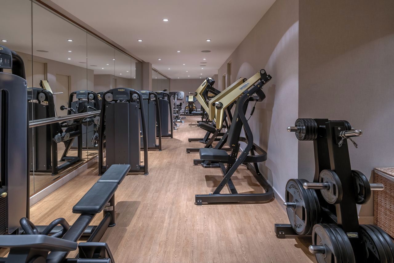 Un gimnasio con diversos equipos de ejercicio, bancos y espejos en las paredes.