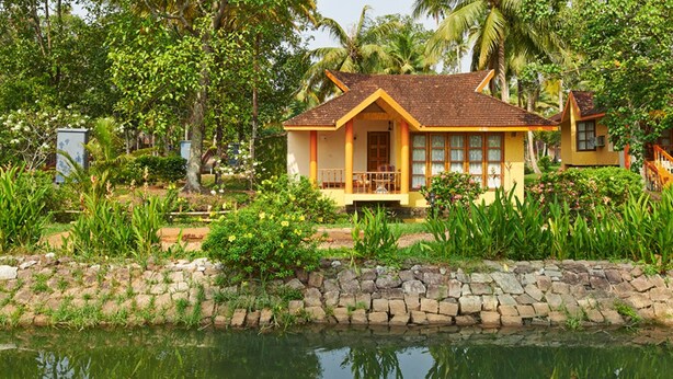 A bungalow with a tiled roof, surrounded by lush greenery and a stone wall. - Club Mahindra Kumarakom (Kottayam)