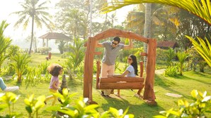 A wooden swing set in a lush garden with palm trees and a gazebo in the background. - Club Mahindra Kumarakom (Kottayam)