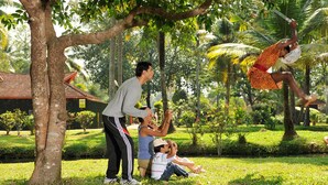 A group of people performing acrobatics in a lush, green outdoor setting with trees and a building in the background. - Club Mahindra Kumarakom (Kottayam)