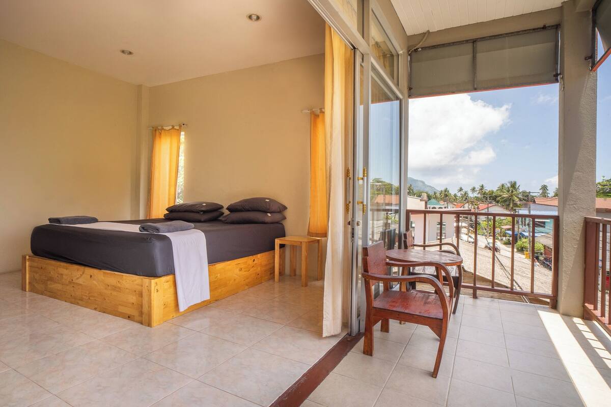 Ein Schlafzimmer mit einem hölzernen Bett, einem kleinen Tisch und einem Balkon mit Blick auf die Stadt.