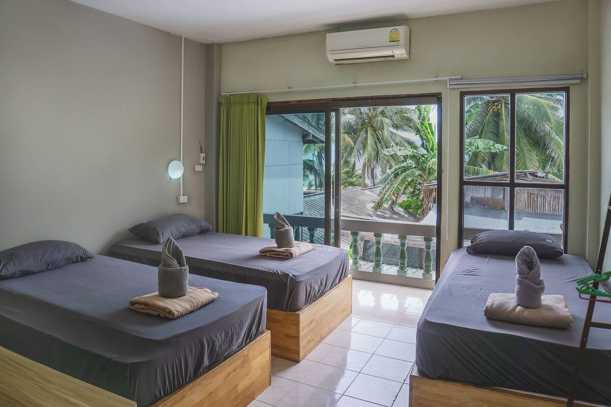 Ein Hotelzimmer mit zwei Betten, einem Balkon mit Blick auf Palmen und einer Klimaanlage an der Wand.