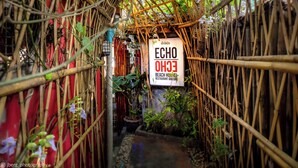 Une arche en bambou mène à un panneau indiquant l’emplacement de l’auberge de jeunesse, du restaurant et du bar « ECHO Beach ».