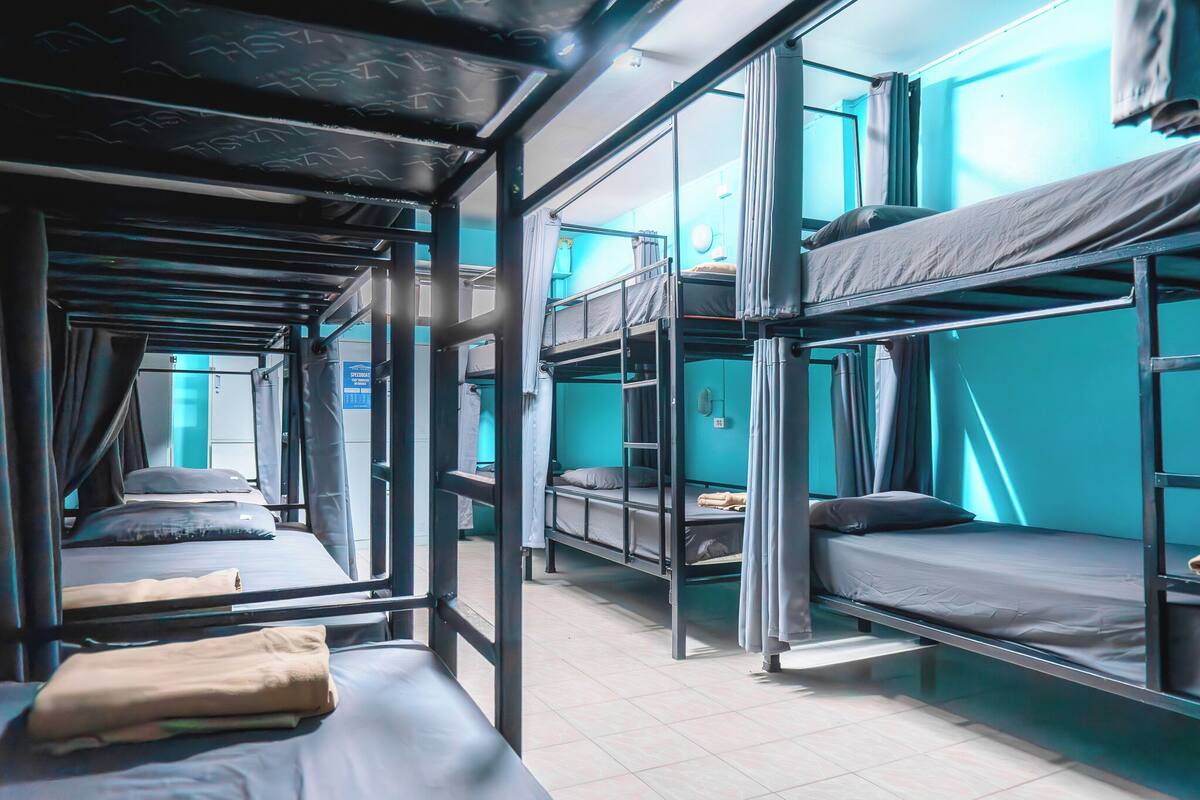 Ein Schlafsaalzimmer mit Etagenbetten, einem Fenster mit Vorhängen und einer sichtbaren Tür.