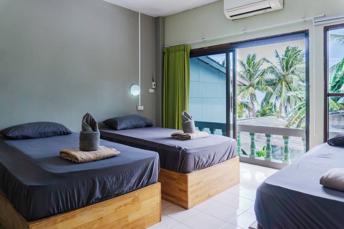 Ein Hotelzimmer mit zwei Betten, einem Balkon mit Blick auf Palmen und einer Klimaanlage an der Wand.