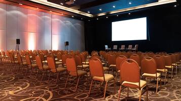A conference room with rows of chairs facing a large screen, carpeted floor, and a stage with chairs.