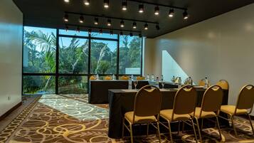 A conference room with a large table, chairs, and a view of tropical vegetation through large windows.