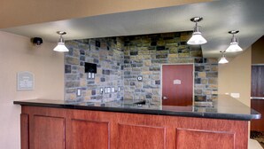 A reception area with a stone wall, a wooden counter, and three pendant lights. - Cobblestone Inn & Suites - Bottineau (Bottineau)