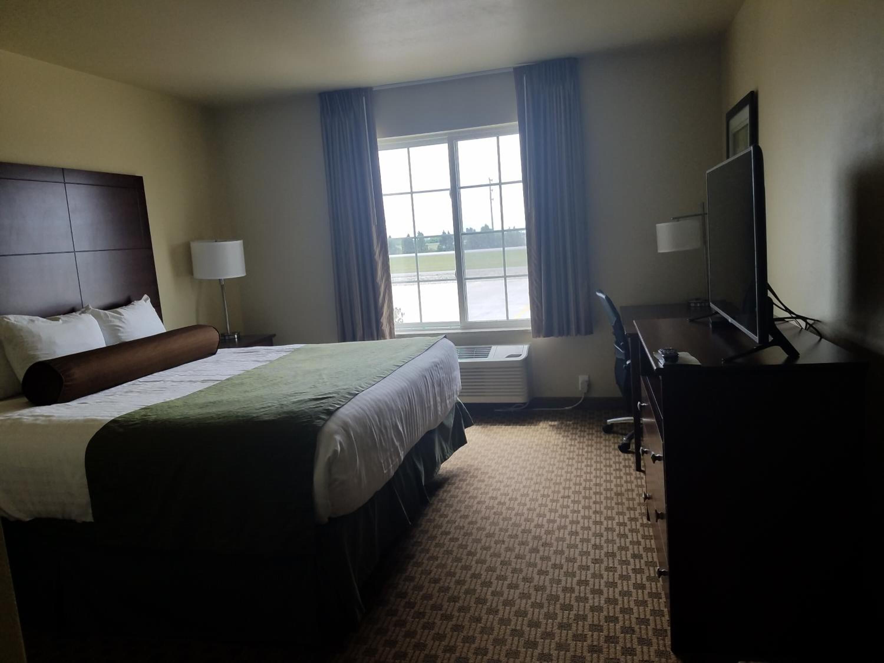 A hotel room with a large bed, a desk with a computer, a TV, and a window with curtains.