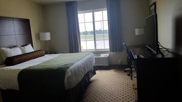 A hotel room with a large bed, a desk with a computer, a TV, and a window with curtains.
