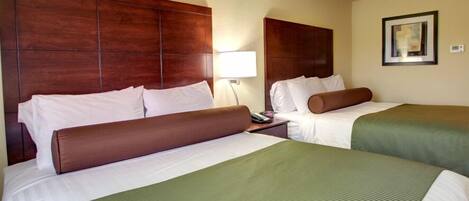 A hotel room with two beds, a wooden headboard, a bedside lamp, and a framed picture on the wall.