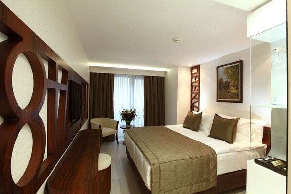 Quarto de hotel com uma cama grande, uma escrivaninha, uma cadeira e um quadro na parede.