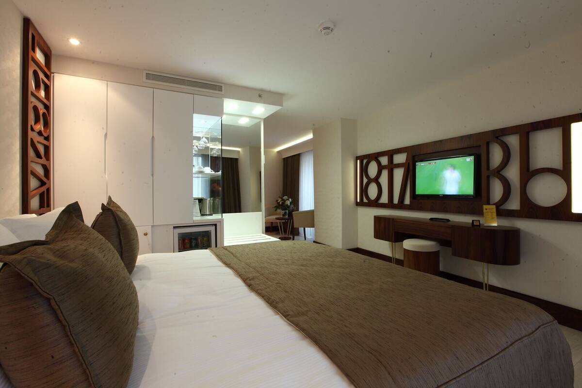 Une chambre d’hôtel moderne dotée d’un grand lit, d’un téléviseur fixé au mur, d’un bureau et d’une petite kitchenette.