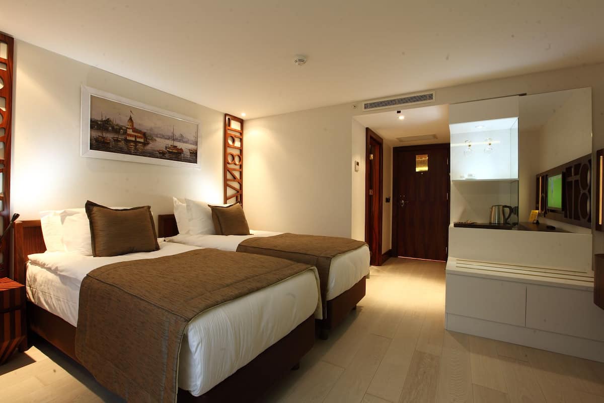 Une chambre d’hôtel avec deux lits, un tableau au mur, une armoire en bois et un téléviseur.