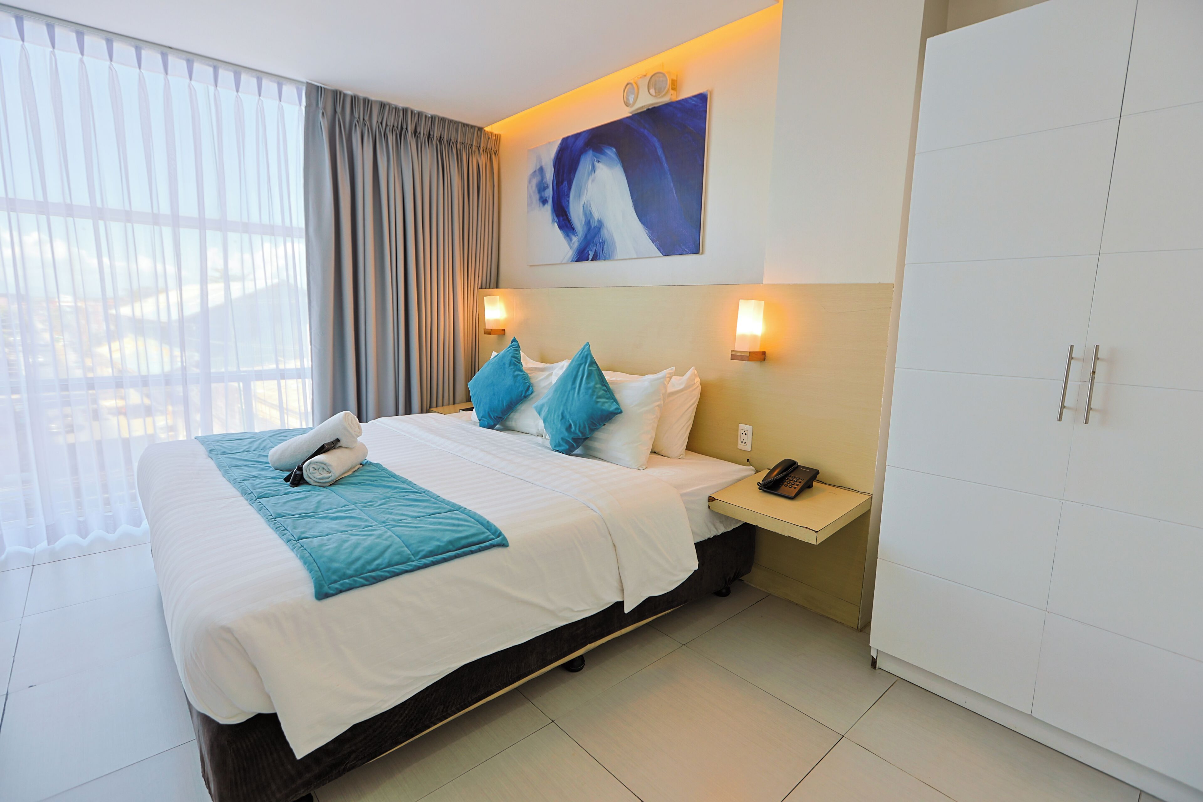 Quarto de hotel com cama, mesa de cabeceira, telefone e um quadro na parede.