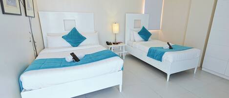 A hotel room with two white beds, each with a blue pillow and blanket, a bedside table with a lamp, and an air conditioning unit on the wall.