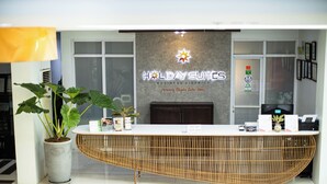 A reception desk with a sign reading "Holiday Suites Business District" and a logo above it. - Holiday Suites Business District (Empire Suites Hotel) (Puerto Princesa)