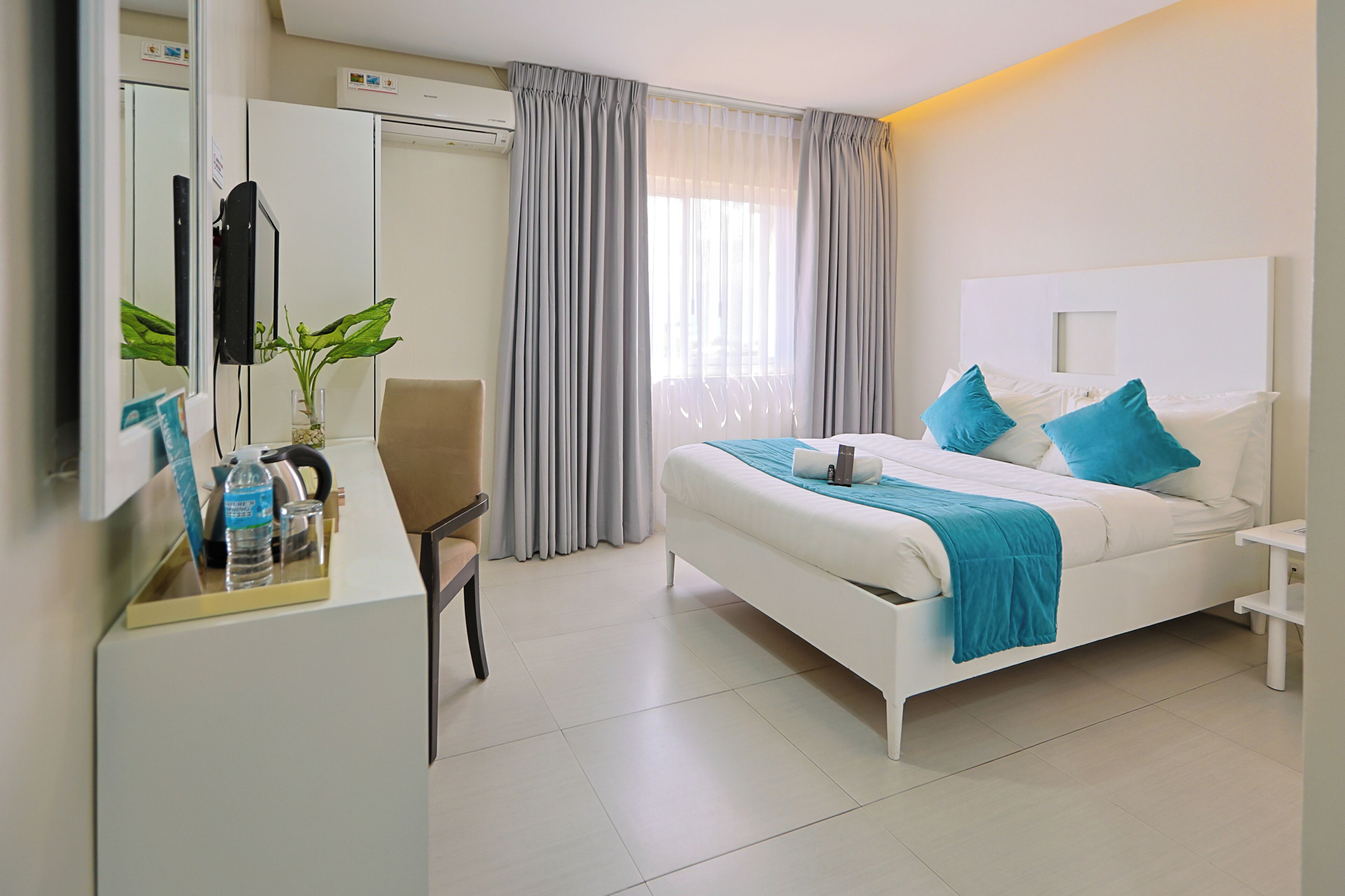 A hotel room with a bed, a desk, a chair, a mirror, and a window with curtains.