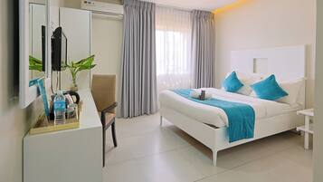 A hotel room with a bed, a desk, a chair, a mirror, and a window with curtains.