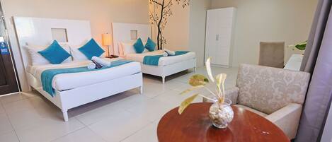 A hotel room with two beds, a sofa, a round table, and a wall-mounted tree decal.