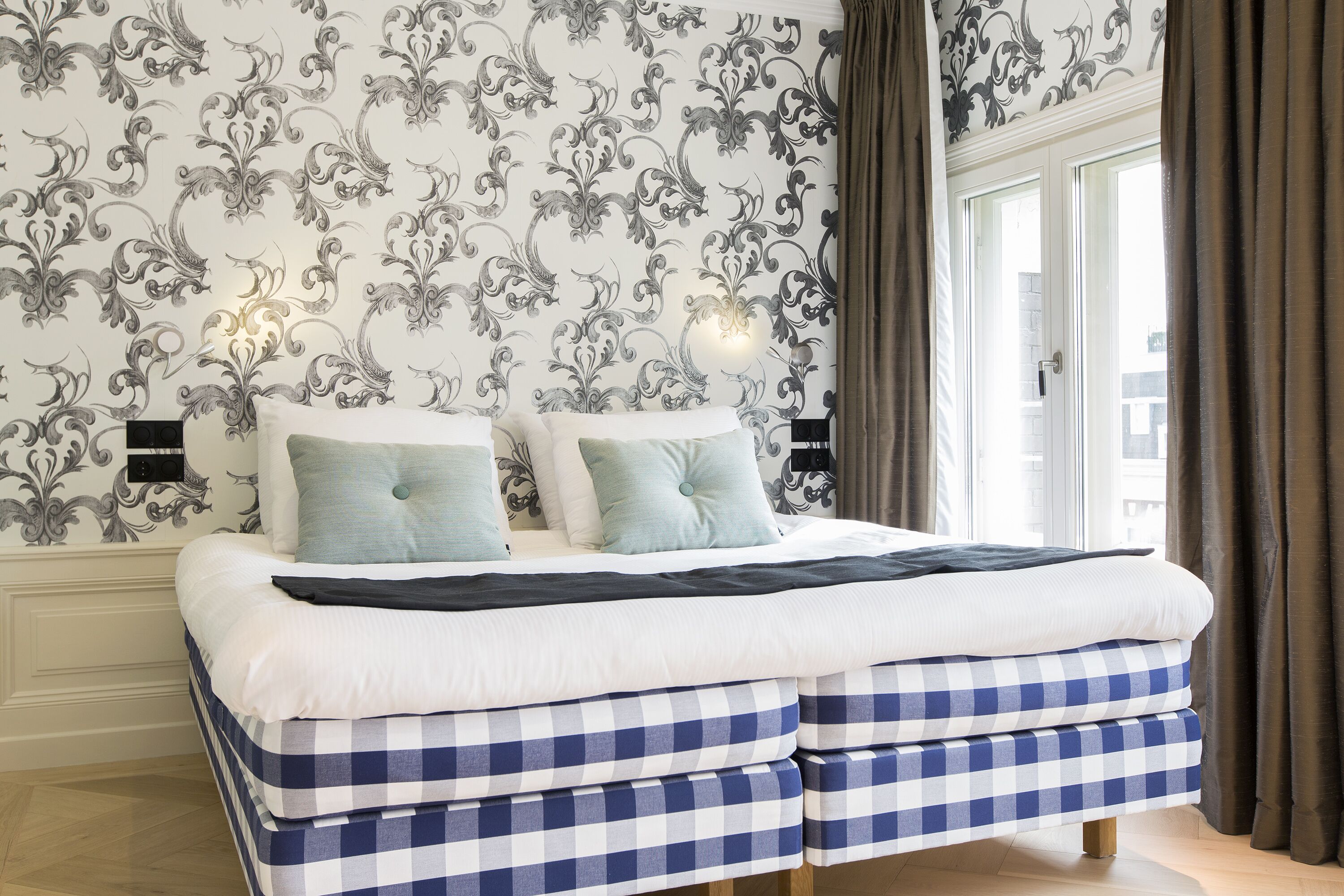 A double bed with a checkered bedspread, two pillows, and a bedside table with a lamp.