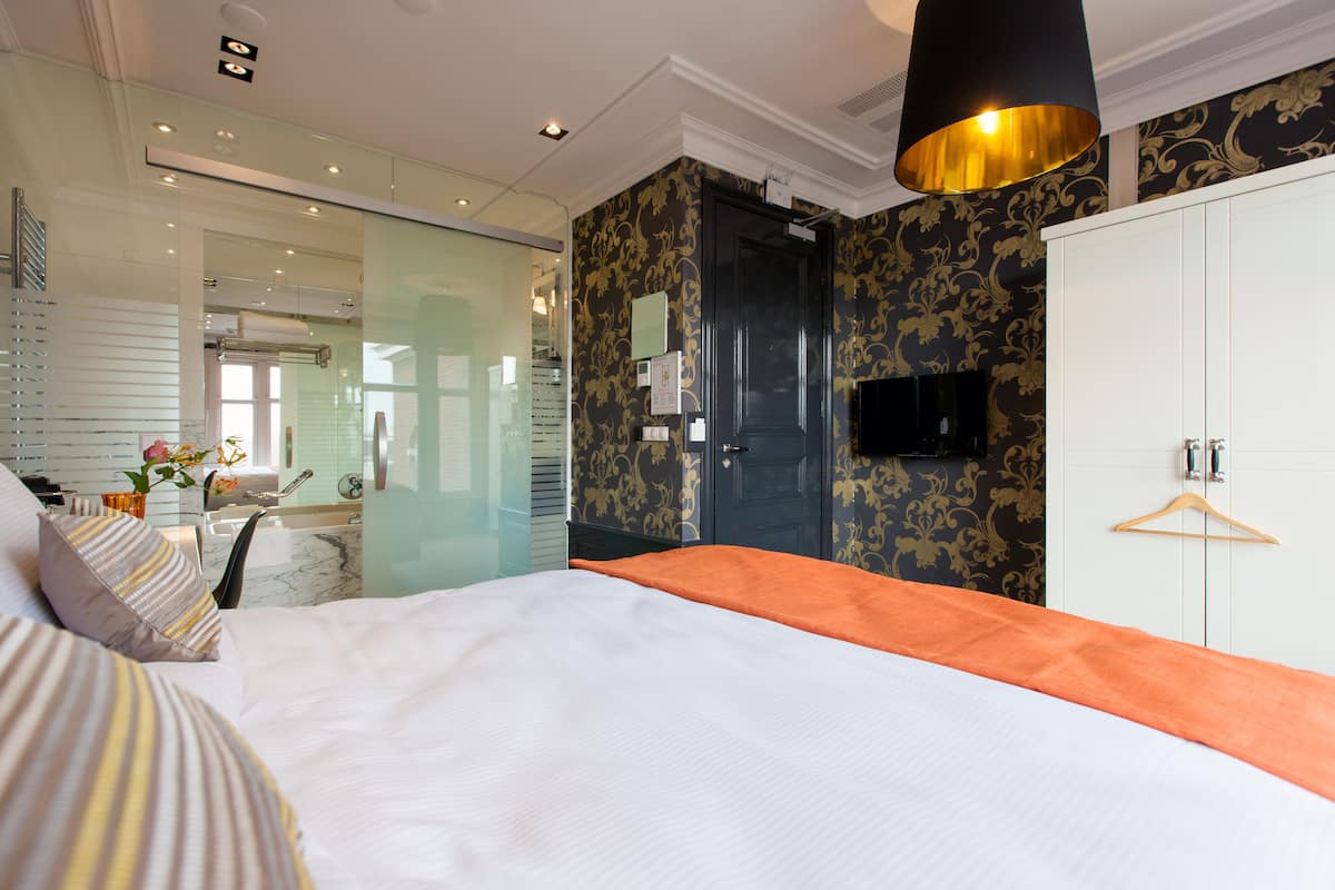Une chambre d’hôtel moderne dotée d’un grand lit, d’une douche à parois de verre, d’une armoire et d’un téléviseur fixé au mur.