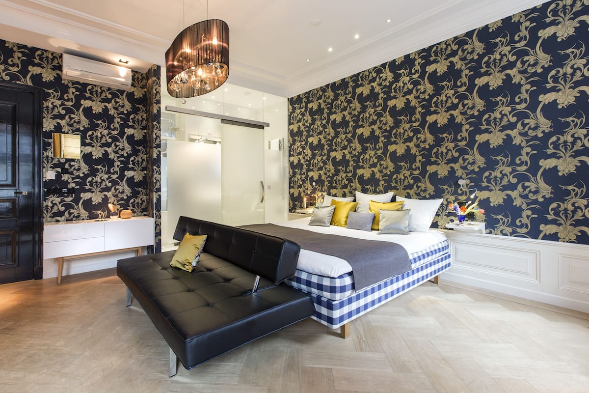 Une chambre à coucher moderne avec un canapé en cuir noir, un lit recouvert d’une courtepointe à carreaux et une table de chevet ornée d’un vase.