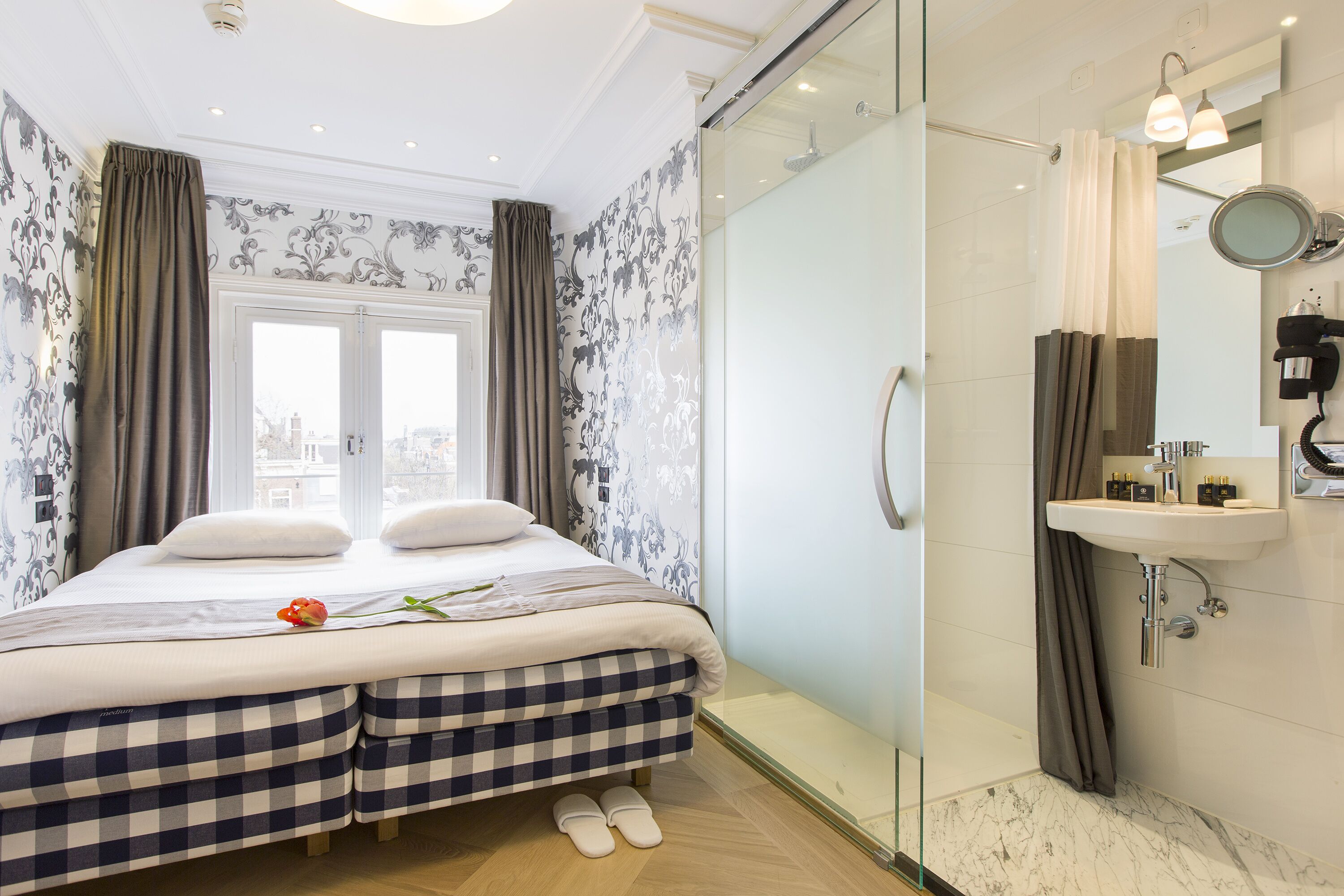 Una habitación de hotel con cama, ducha y baño completo con lavamanos y espejo.