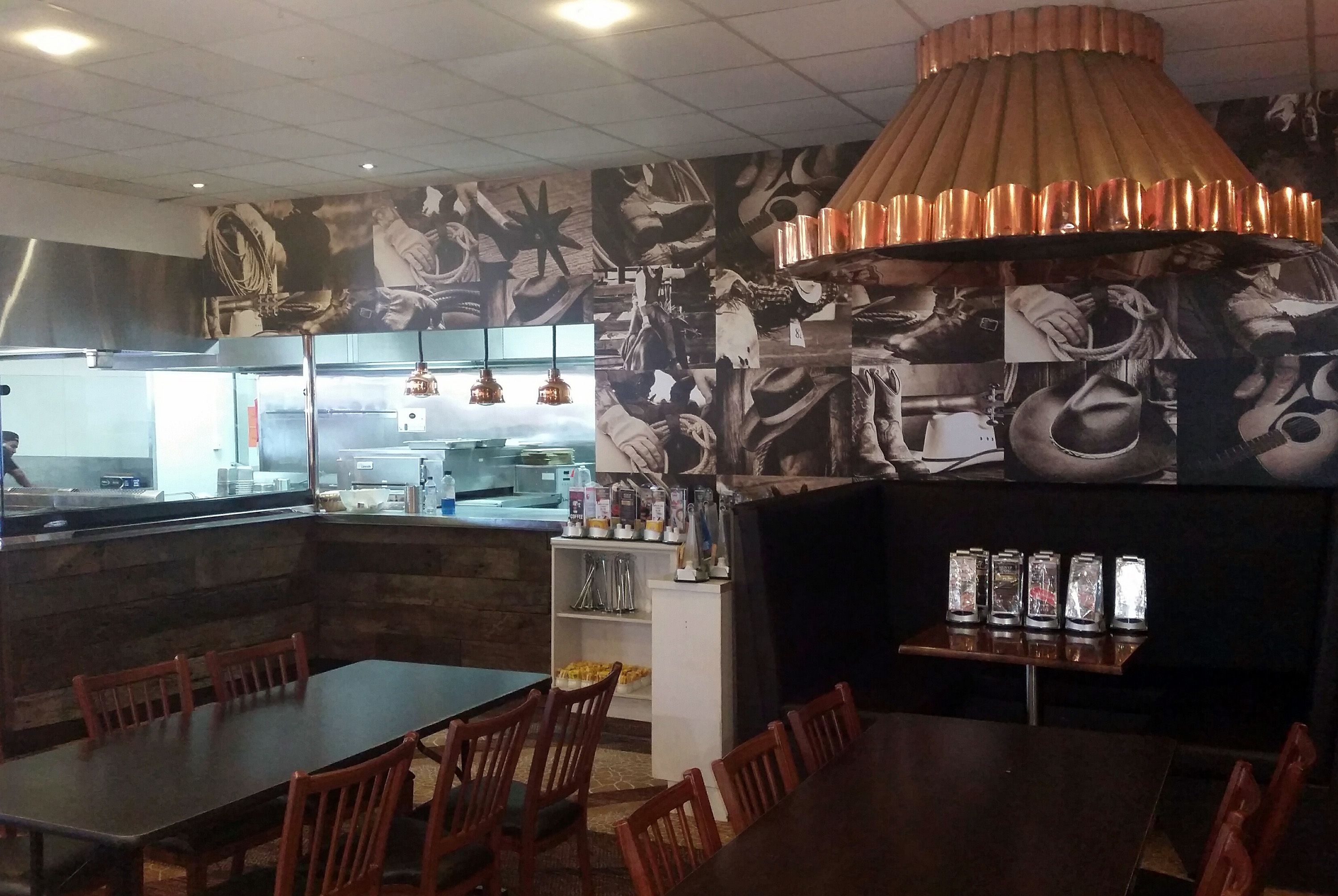 Interior de un restaurante con mesas y sillas de madera, una isla central con mostrador y una lámpara decorativa de gran tamaño.