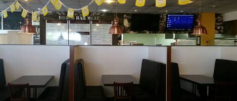 Interior de restaurante con cabinas, una pizarra de menú y pancartas amarillas.