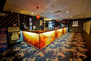A bar area with a patterned carpet, a counter with a digital display, and a wall with various signs and a menu board.