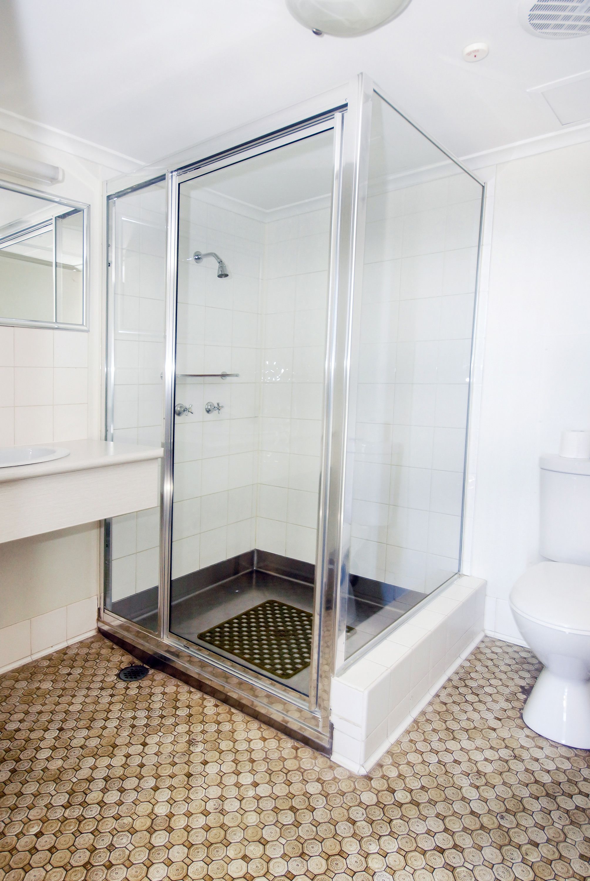 Un baño con ducha de vidrio, inodoro blanco y piso de baldosas con un diseño único.