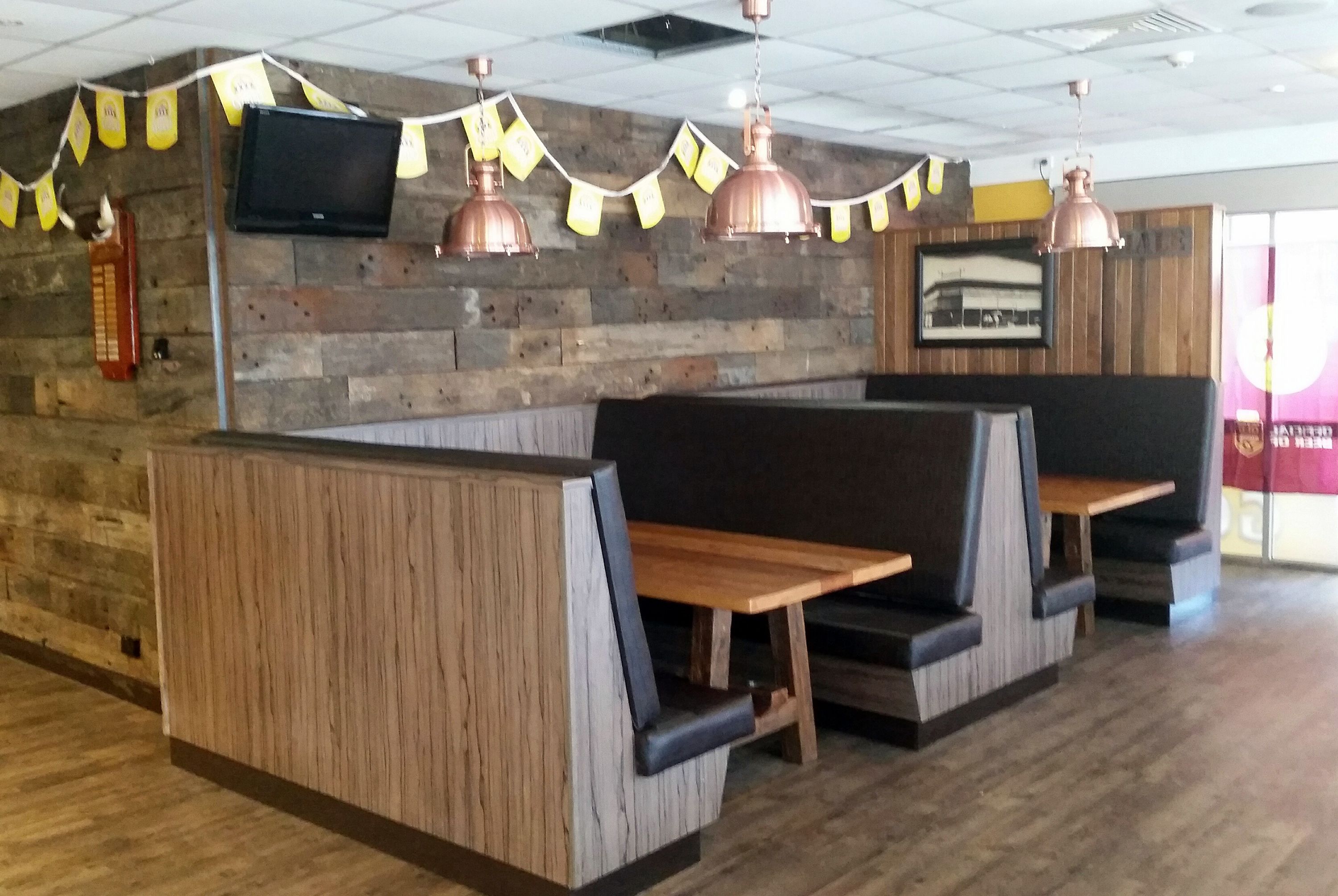 A restaurant interior with wooden panel walls, metal pendant lights, and cushioned booths.