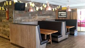 A restaurant interior with wooden panel walls, metal pendant lights, and cushioned booths.