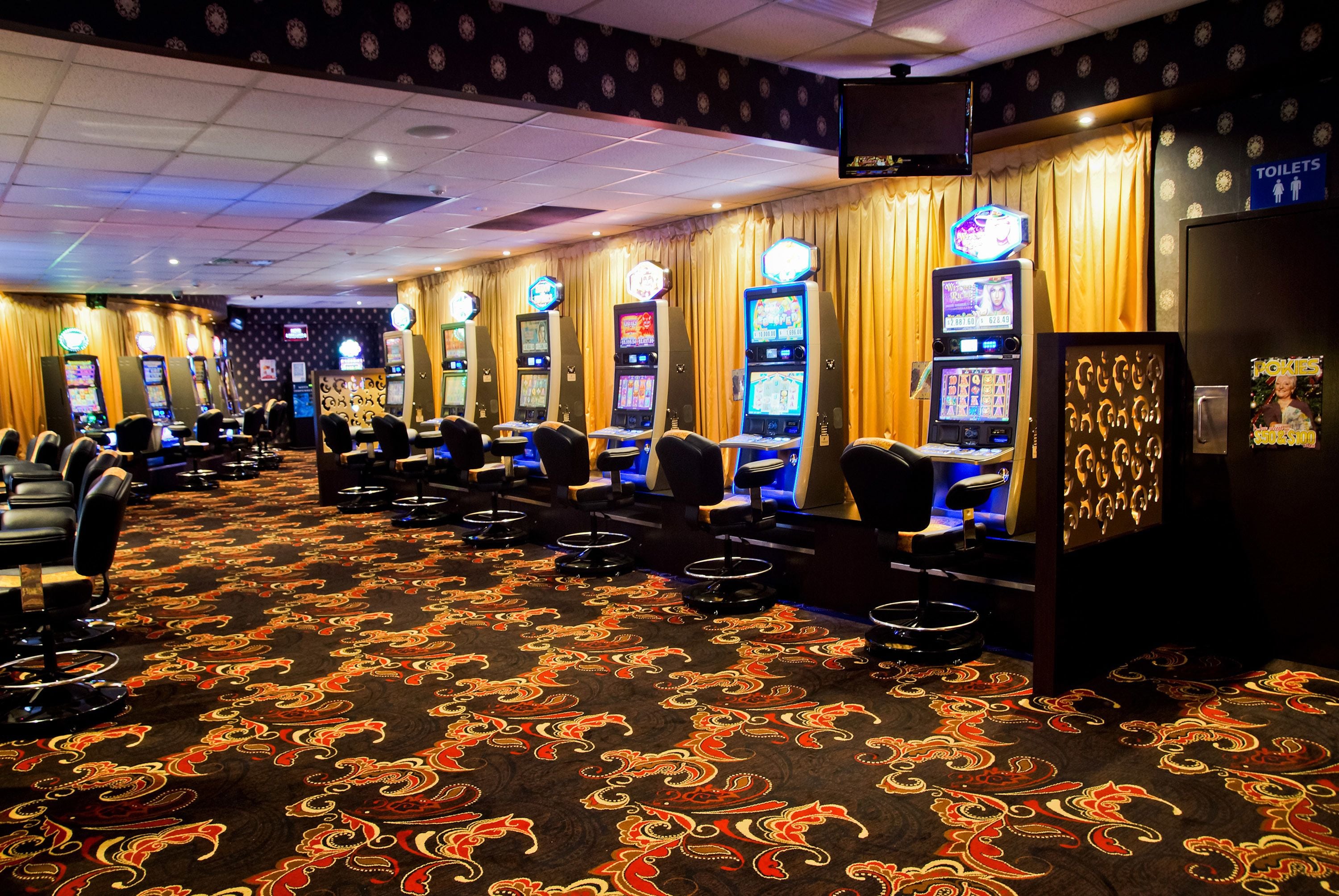 A casino floor with slot machines, chairs, and a carpet with a paisley pattern.