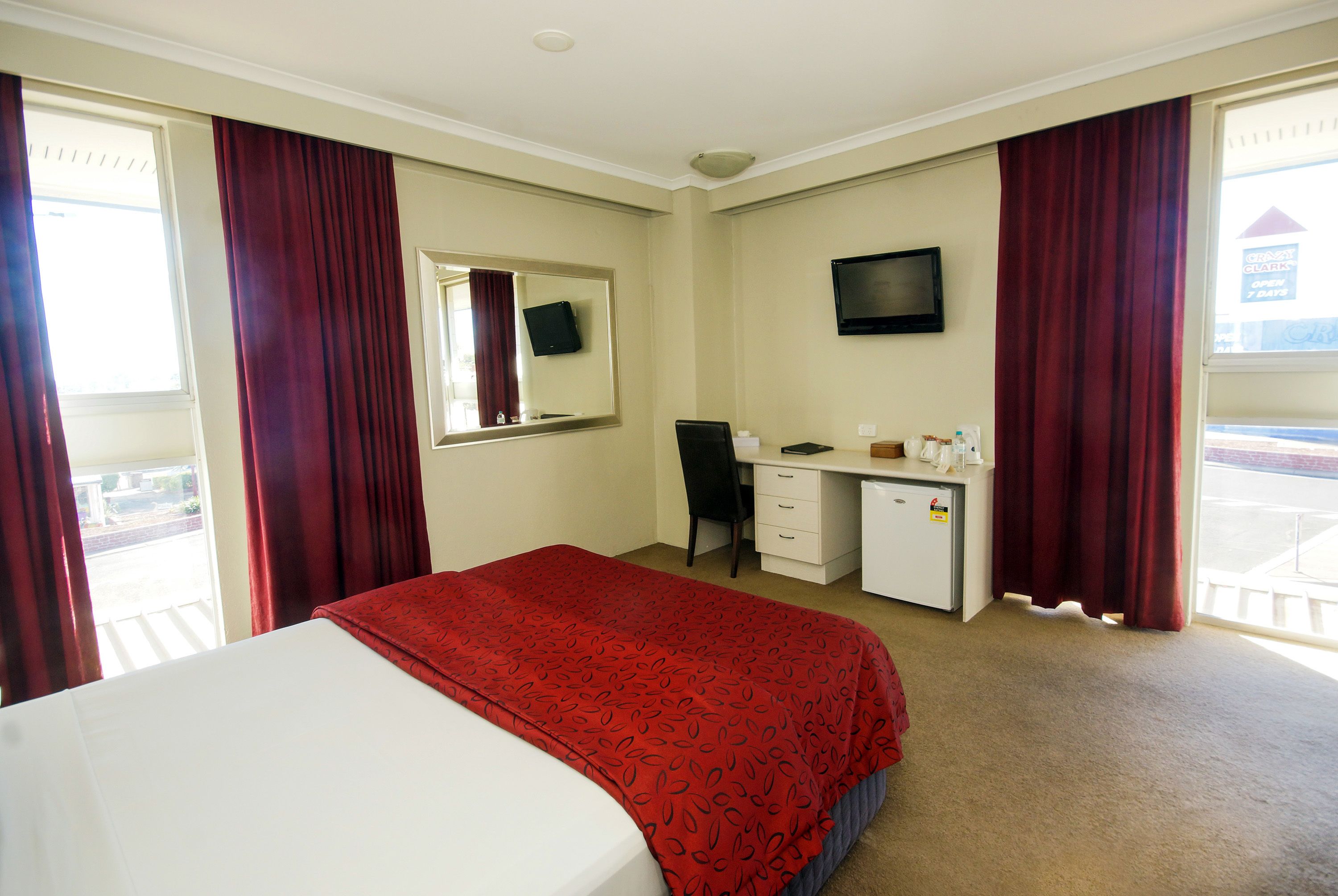 Una habitación de hotel con cama, escritorio, silla y televisión en la pared.