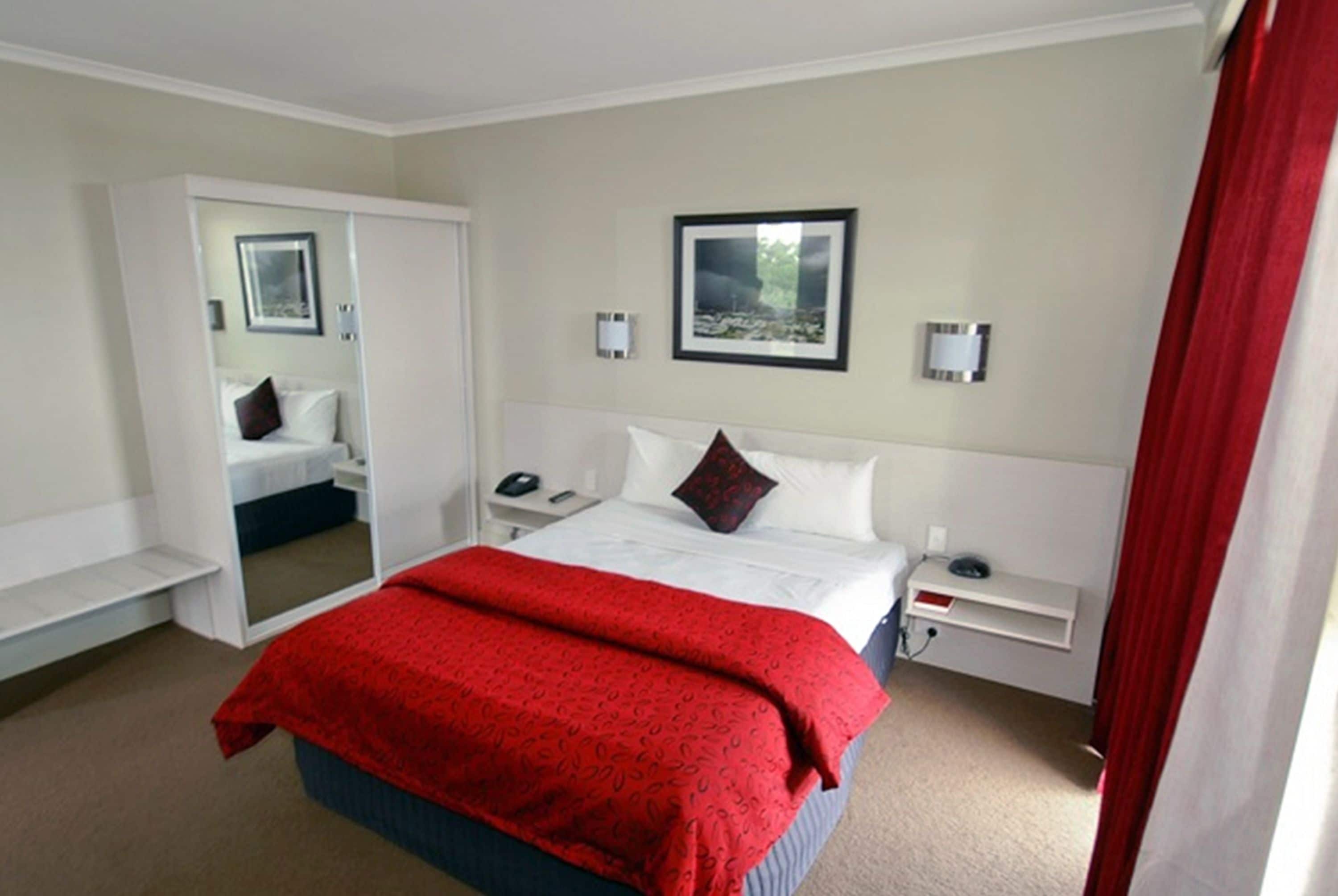 Una habitación de hotel con cama, mesitas de noche, espejo y un cuadro en la pared.