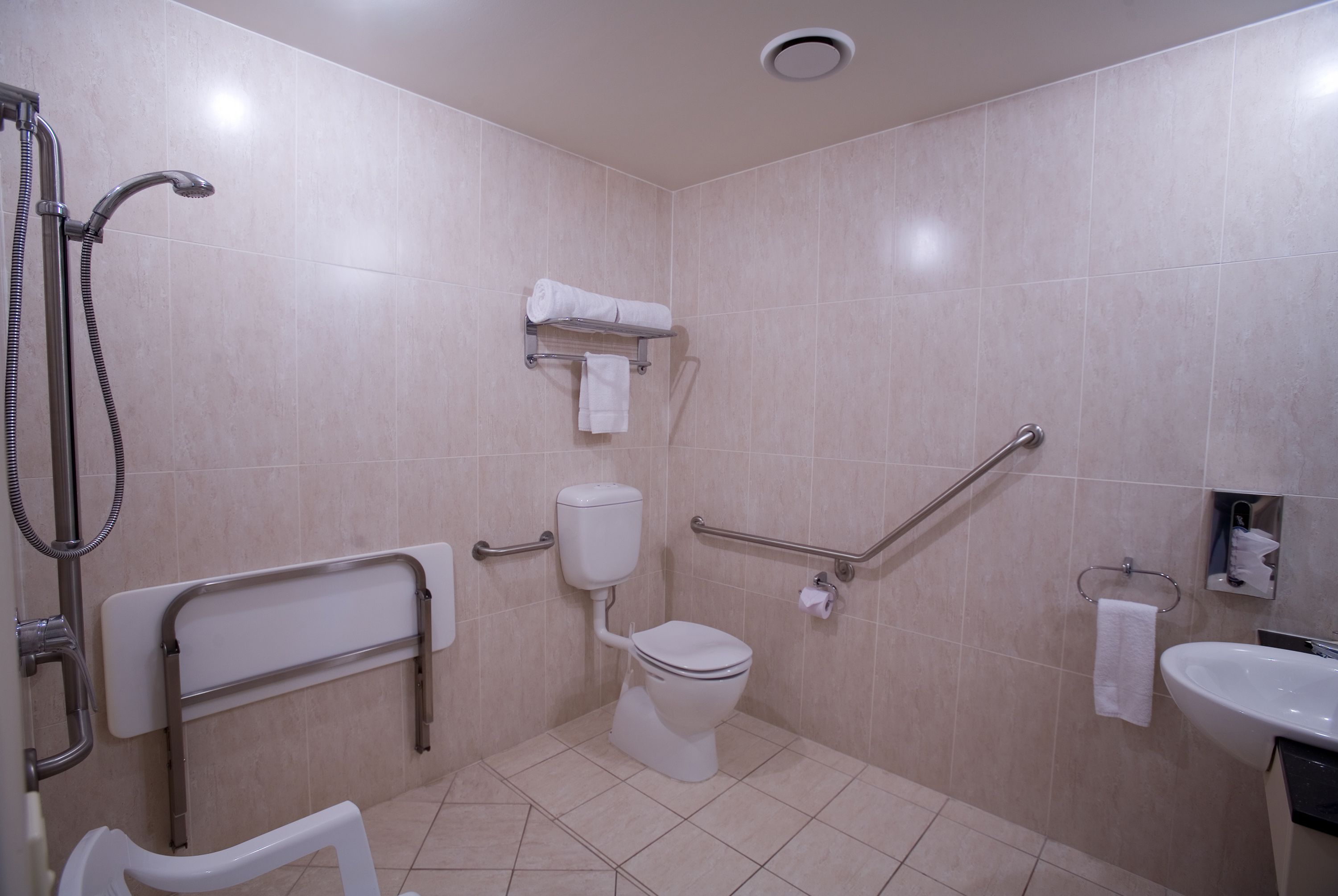 A bathroom with a toilet, shower, grab bars, and a sink.