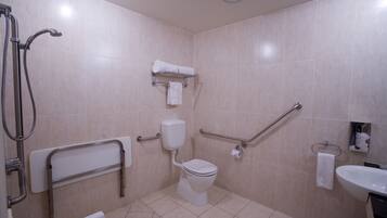 Un baño con inodoro, ducha, barras de apoyo y lavamanos.