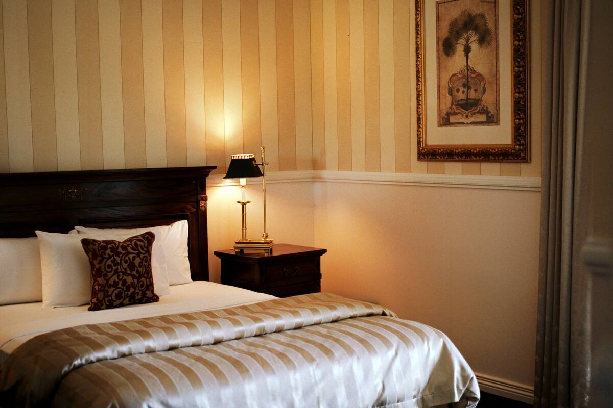 Una cama bien hecha con ropa de cama a rayas, una lámpara de noche y un cuadro en la pared.