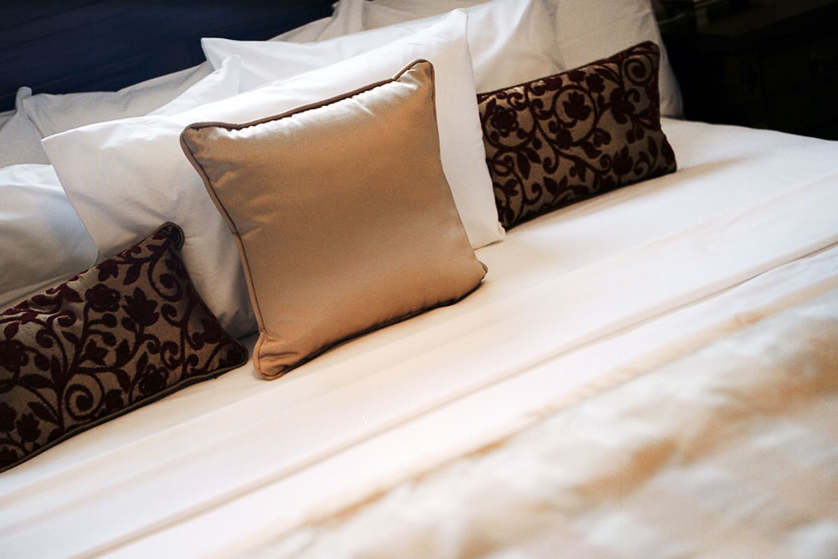Una cama bien tendida con almohadas blancas y estampadas.