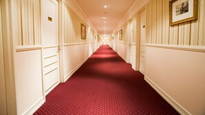 A hotel hallway with a red carpet, white walls, and doors with gold handles. - Redearth Hotel (Mount Isa City)