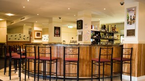 A bar area with a wooden counter and black bar stools. There are shelves with bottles and glasses behind the counter. - Redearth Hotel (Mount Isa City)