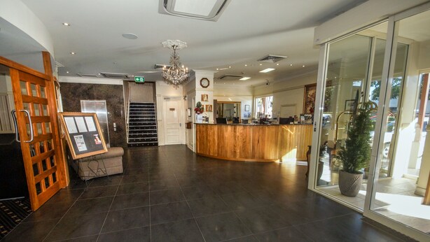 A reception area with a wooden counter, a chandelier, and a potted plant. - Redearth Hotel (Mount Isa City)