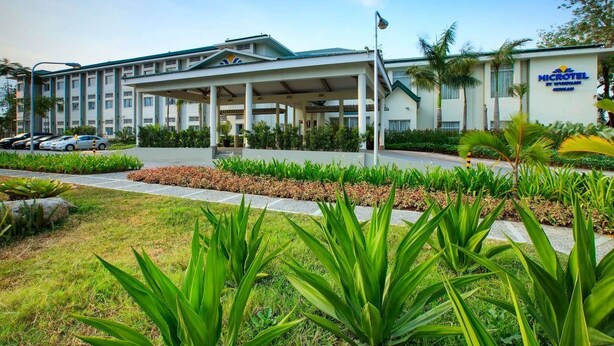Un hotel Microtel con entrada techada, zona de estacionamiento y jardines bien cuidados.